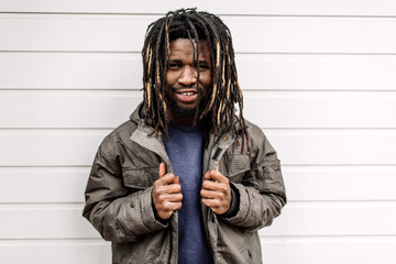 Wall Mural - Beautiful African American with dreadlocks, pigtails hair in brown trousers and blue sweater against the background of houses, city