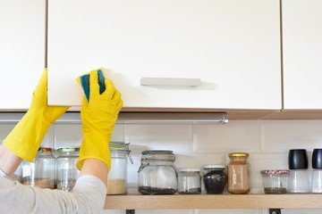 woman in yellow gloves washes the door in kitchen cabinet