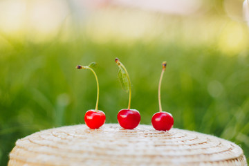 few ripe fruits of sweet cherry with twig on straw hat lying on the grass outdoors. Picnic on nature in the park close up healthy food, diet, personal care. sunny day.