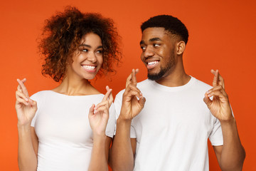 Cute black man and woman with crossed fingers making wish