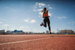 © Comeback Images - From below back view of teen girl in sportswear sprinting on running track at stadium under blue sky on summer day