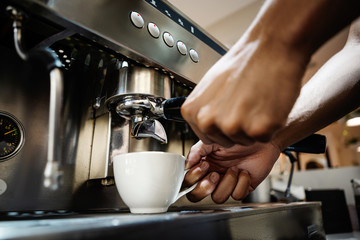 Closeup crop hands of bartender pouring coffee into cup from coffee machine at counter in coffee shop