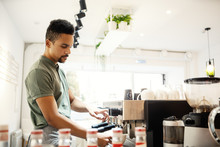 Side View Of Young Concentrated Bartender Pouring Coffee Into Cup From Espresso Machine At Counter In Small Coffee Shop
