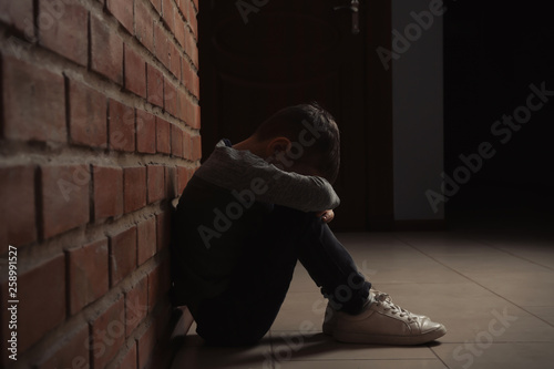 Sad little boy sitting on floor near brick wall indoors Tableau sur Toile