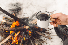 Male Hands Hold A Mug Of Coffee Near A Burning Campfire. Concept Hike, Walk, Trip In Winter.