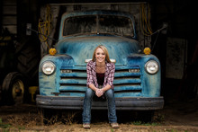 Attractive Young Woman Sitting On The Bumper Of An Old Truck