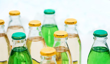 Small Bottles With Lemonade Under The Caps, Yellow And Green, Stand In A Row Against A White Background.