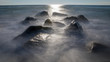 Misty, moody rocks on the shore at sunrise with the sun reflecting off the ocean. Photo by: Chuck Beyer