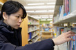 © Kenishirotie - Portrait of serious Asian lady in library looking for a book