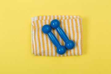 Styled photography of fitness equipment dumbbells  and towel on yellow background.