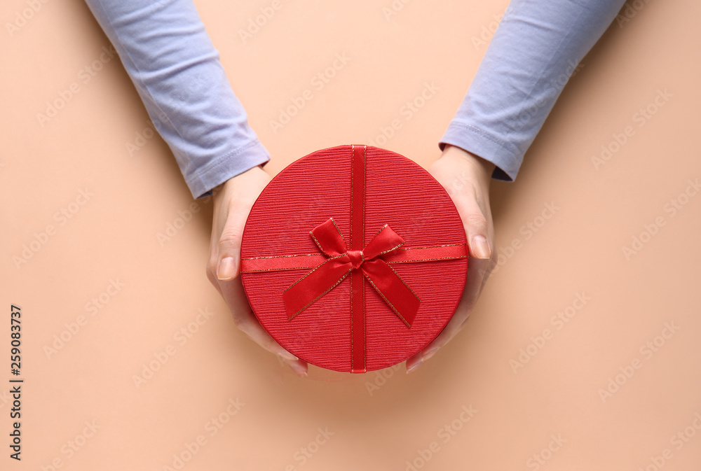 Female hands with gift box on color background