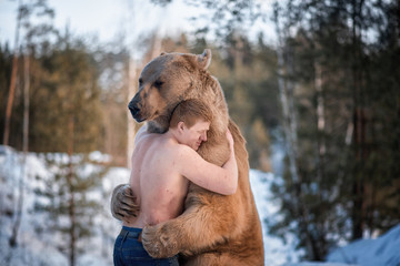 half-naked man hugs a brown bear in a winter forest. bear hugs man in response. the theme of the fri