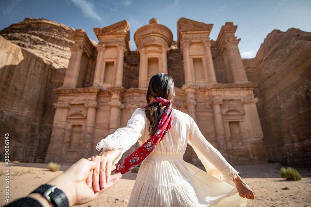 Asian woman tourist in white dress holding her couple hand at Ad Deir or El Deir, the monument carved out of rock in the ancient city of Petra, Jordan. Travel UNESCO World Heritage Site in Middle East - obrazy, fototapety, plakaty 