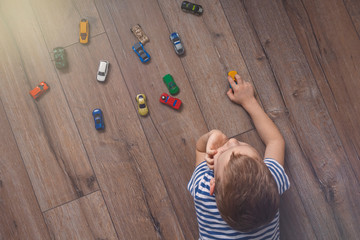 Child playing with miniature toy cars on wooden floor. Top view