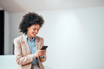 beautiful smiling curly-haired businesswoman using smarphone indoors, copy space.