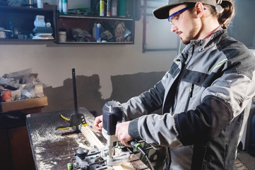 Portrait of a young carpenter joiner with electric milling cutter in the hands of a worker in a home workshop. Starting a business. Craftsman