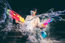 Young Asian Men Are Laughing Fun On Songkran Festival. He Was Holding A Large Squirt Guns In Both Hands, And In The Midst Of The Water Is Splashed Out Around The Direction. On A Black Background.