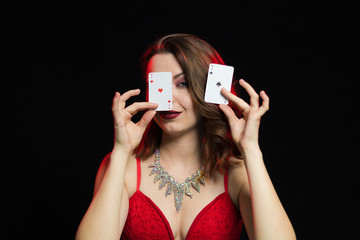 Emotional young lady in an evening red dress playing cards on a table on green cloth in a casino