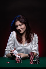 Brunette actress girl plays cards over green cloth posing on a dark background in blue and red light.