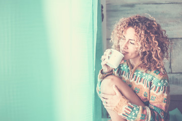 Wall Mural - Happy quiet and peaceful young attractive woman enjoy the relax time at home drinking a cup of tea and looking outside the window - curly hair for caucasian people