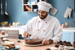 Male confectioner decorating tasty chocolate cake in kitchen