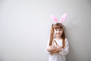 Wall Mural - Cute little girl with Easter eggs and bunny ears on light background