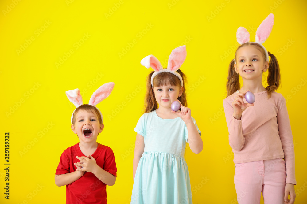 Cute little children with Easter eggs and bunny ears on color background
