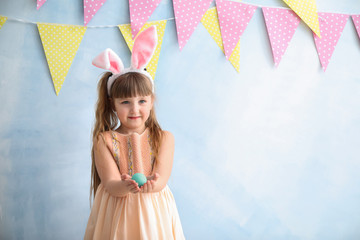 Wall Mural - Cute little girl with Easter egg and bunny ears near color decorated wall