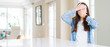 © Krakenimages.com - Wide angle picture of beautiful young woman sitting on white table at home Covering eyes and mouth with hands, surprised and shocked. Hiding emotion