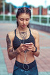 © byswat - Beautiful girl athlete summer city with tattoo cat. In his hand, phone listens music headphones. Rest after training, online application in Internet. Motivation sports, lifestyle. Active lifestyle.