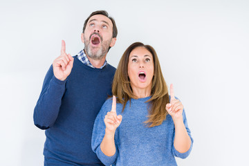 Poster - Beautiful middle age couple in love over isolated background amazed and surprised looking up and pointing with fingers and raised arms.