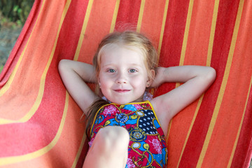 Concept summer, vacation, weekend- beautiful blond-haired girl with blue eyes is lying on a bright hammock with rainbow colors