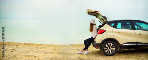 Fotografía View of young woman traveler looking at sea sunset, sitting on hatchback car with the copy space