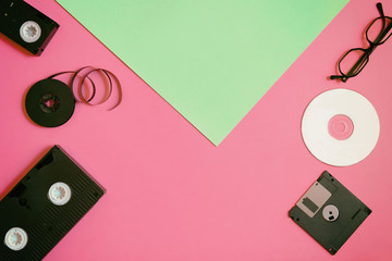 Retro storage devices: plate, two videocassette, floppy disk, CD and glasses. Outdated technology concept on pink and mint paper background, top view, minimalism