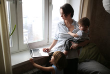 Mom With Children Working On Laptop Near Window