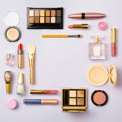 Wall Mural - Square image of cosmetics for social media with empty place for text. Woman make up cosmetics on purple. Copy space. Gold and purple decorative cosmetic: highlighter, concealer, rouge, eye shadows etc