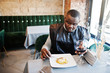 © AS Photo Family - African man in black traditional clothes sitting at restaurant and eat pasta and drink wine.