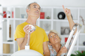 elderly grey-haired couple repairs lamp under ceiling