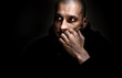 Dramatic dark portrait with strong contrast and film grain of young man sitting in the room with sadness and depression in his eyes thinking about life