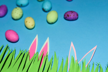 Grass With Rabbit Ears And Candy Eggs On Blue