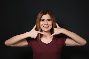 Wall Mural - Woman showing CALL ME gesture in sign language on black background