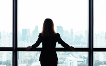 Asian Business Woman Standing And Looking Out The Window At City View Background