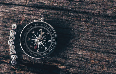 Compass on wood deck with blocks of letters making the word survival.