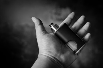 black and white, monochrome shot of high end unregulated bottom feed squonk box mods with rebuildable dripping atomizer in hand, vaping device, selective focus