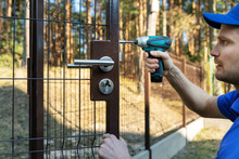 Worker Installing The Lock For New Metal Fence Gates