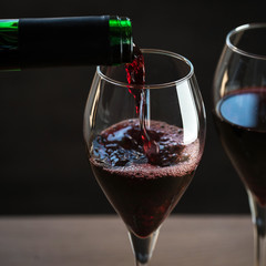 Wall Mural - Pouring red wine into the glass against wooden background