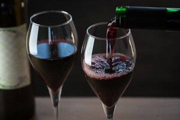 Wall Mural - Pouring red wine into the glass against wooden background