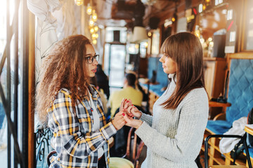 Two teenage girls holding hands and smiling while standing in cafeteria.