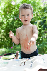 Little boy is having fun painting with paints on the street in summer