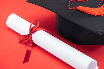 Wall Mural - Academic cap with tassel and diploma with ribbon on red surface